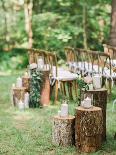 an outdoor wedding setup with candles, flowers and greenery on wooden stumps in the grass