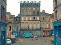 an old building with people walking around in the street and cars parked on the side