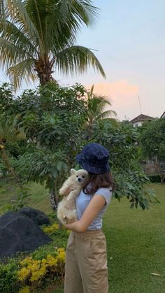 a woman holding a teddy bear in her arms while standing next to a palm tree