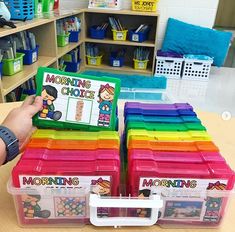 a person holding up a box filled with different colored plastic containers in front of bookshelves