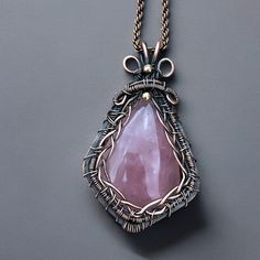 a necklace with a large pink stone hanging from it's side on a gray surface