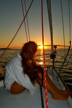 a woman sitting on the back of a sailboat at sunset with her legs crossed