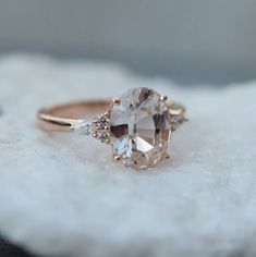 a ring with an oval cut diamond and three smaller round diamonds on the side, sitting on top of a white cloth