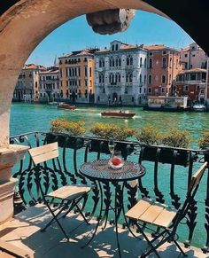 an outdoor table and chairs on a balcony overlooking a canal with boats in the water