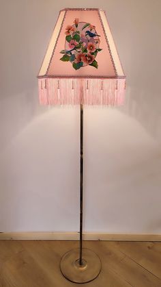 a floor lamp with a pink shade and flowers on the bottom, sitting on a wooden floor