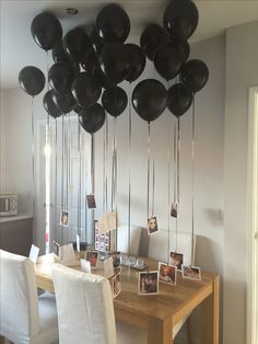 black balloons are hanging from the ceiling above a dining room table with white chairs and pictures on it