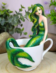 a green mermaid figurine sitting in a teacup