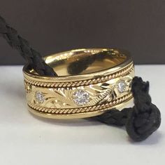 two gold rings with diamonds on them sitting next to a black rope and knoted cord