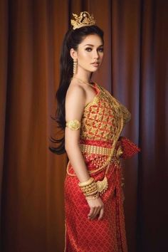 a woman in a red and gold dress with a crown on her head standing next to a curtain