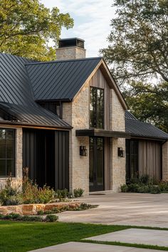 a house with a black metal roof and stone walls on the front lawn, surrounded by trees