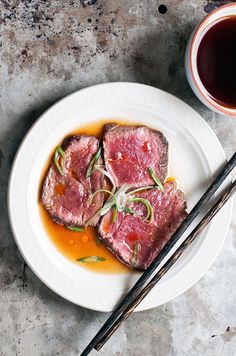 two pieces of meat on a plate with chopsticks next to it and a cup of tea