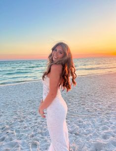 a woman standing on top of a sandy beach next to the ocean in a white dress