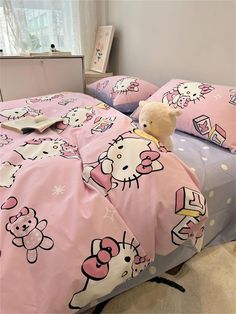 a bed with hello kitty sheets and pillows on it, next to a stuffed animal