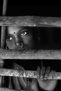 a woman with piercings peeking out from behind a wooden fence in black and white