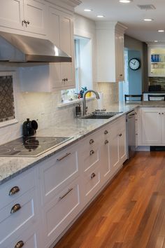 a large kitchen with white cabinets and wood flooring, along with a clock on the wall