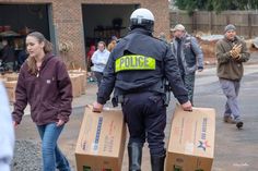 two police officers carrying boxes in front of a group of people walking down the street