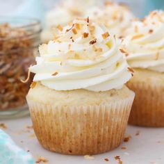 three cupcakes with white frosting and sprinkles on top, next to a bowl of granola