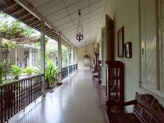 a long hallway with lots of windows and wooden furniture on the side walk between two buildings