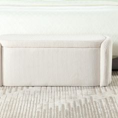 an upholstered bench sits on the floor in front of a bed with white sheets and pillows