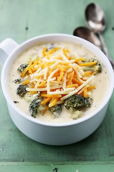 a white bowl filled with broccoli cheese soup on top of a green table