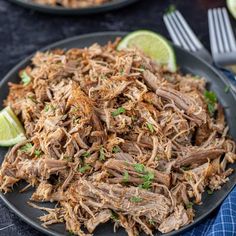 shredded pork on a black plate with lime wedges and fork next to the plate