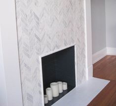 three candles are placed in front of a fireplace with white herringbone tiles on it