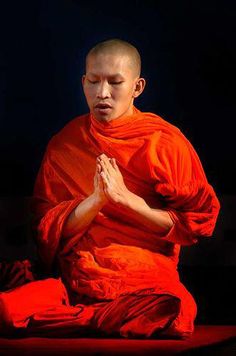 a man sitting on the ground with his hands folded in front of him while wearing an orange outfit