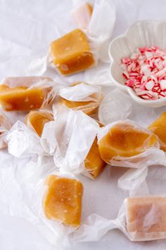 several pieces of candy sitting on wax paper next to a bowl with candy canes