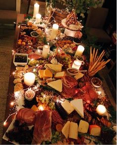 a table covered in lots of different types of cheeses and meats with lit candles