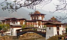 a bridge over a river in front of a large white building with red roof tops