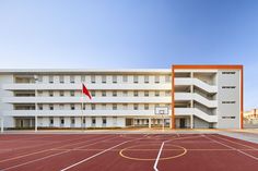 an empty basketball court in front of a white building with a red flag on it