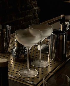 three martini glasses sitting on top of a metal tray next to bottles and silver cups