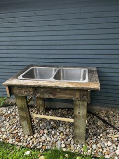 an old wooden table with two sinks on it in front of a gray wall and green grass