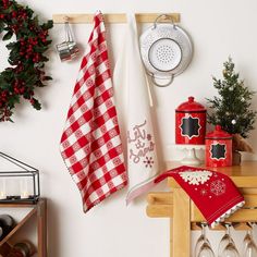 red and white kitchen towels hanging on the wall next to utensils, pot holders and christmas decorations