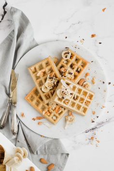 waffles with bananas and nuts on a white plate next to a silver fork