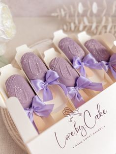 six lavender cake pops in a white box with purple ribbon and bow on the top