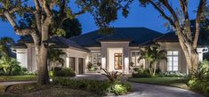 a large house with lots of trees and bushes in front of it at night time