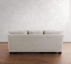 a white couch sitting on top of a wooden floor next to a wall and window