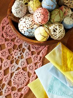 a bowl filled with lots of different colored eggs on top of a wooden table next to crocheted doily