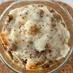 a glass bowl filled with food on top of a cork board covered in gravy