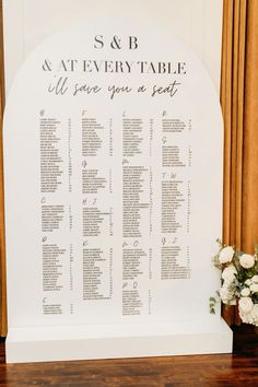 the seating chart for this wedding ceremony is displayed on a wooden table with white flowers and greenery