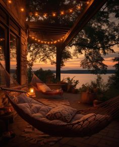 a hammock with pillows and lights hanging from it on a porch overlooking the water