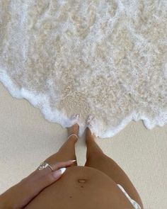 a woman laying on the beach with her feet in the sand and water behind her