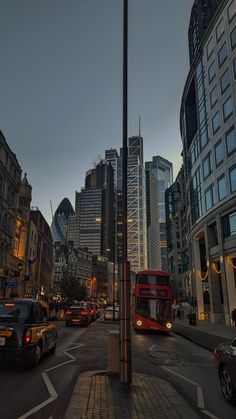 a red double decker bus driving down a street next to tall buildings and traffic lights