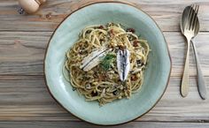 a plate of pasta with parmesan cheese and fish on it next to silverware