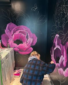 a woman painting flowers on a wall with purple and pink colors in an art studio