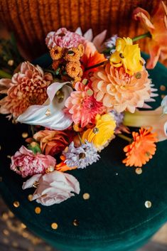 an arrangement of flowers on top of a green velvet chair with gold confetti