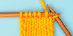 an orange knitted piece with two knitting needles next to it on a blue surface