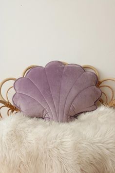 a purple scallop pillow sitting on top of a white fur covered bed headboard