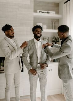 three men in suits are standing together and fixing the tie on another man's suit